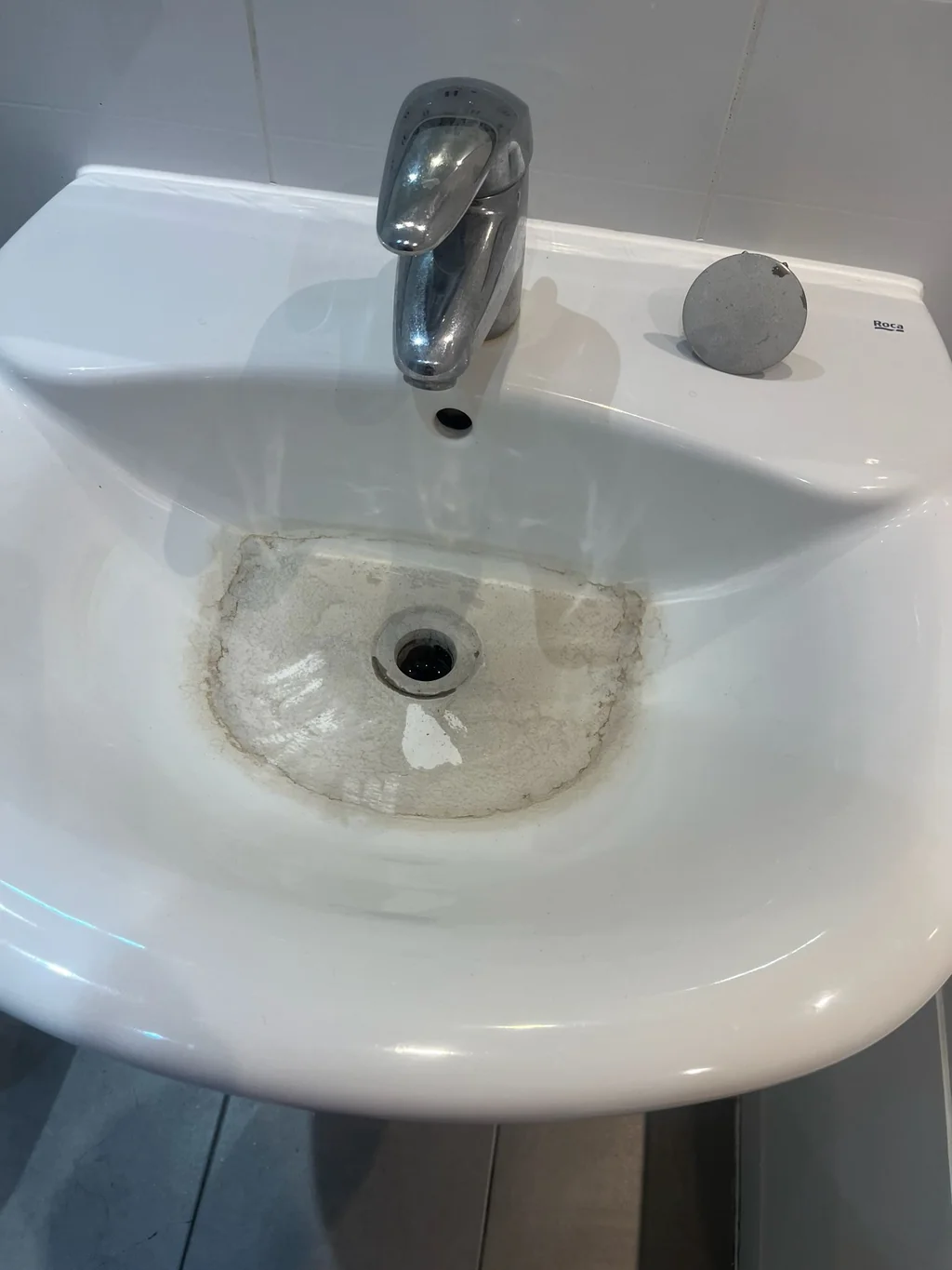 Pedestal basin with a grey limescale ring before cleaning